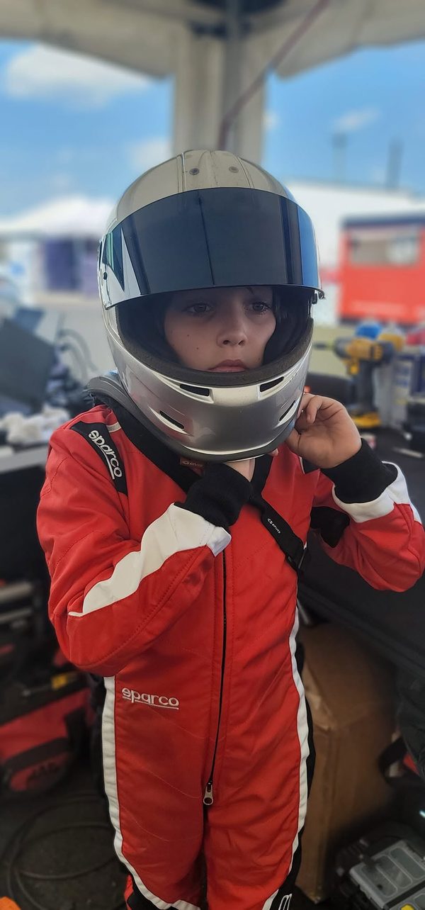 Parker Ives in his Sparco race suit, fastening his helmet in the paddock